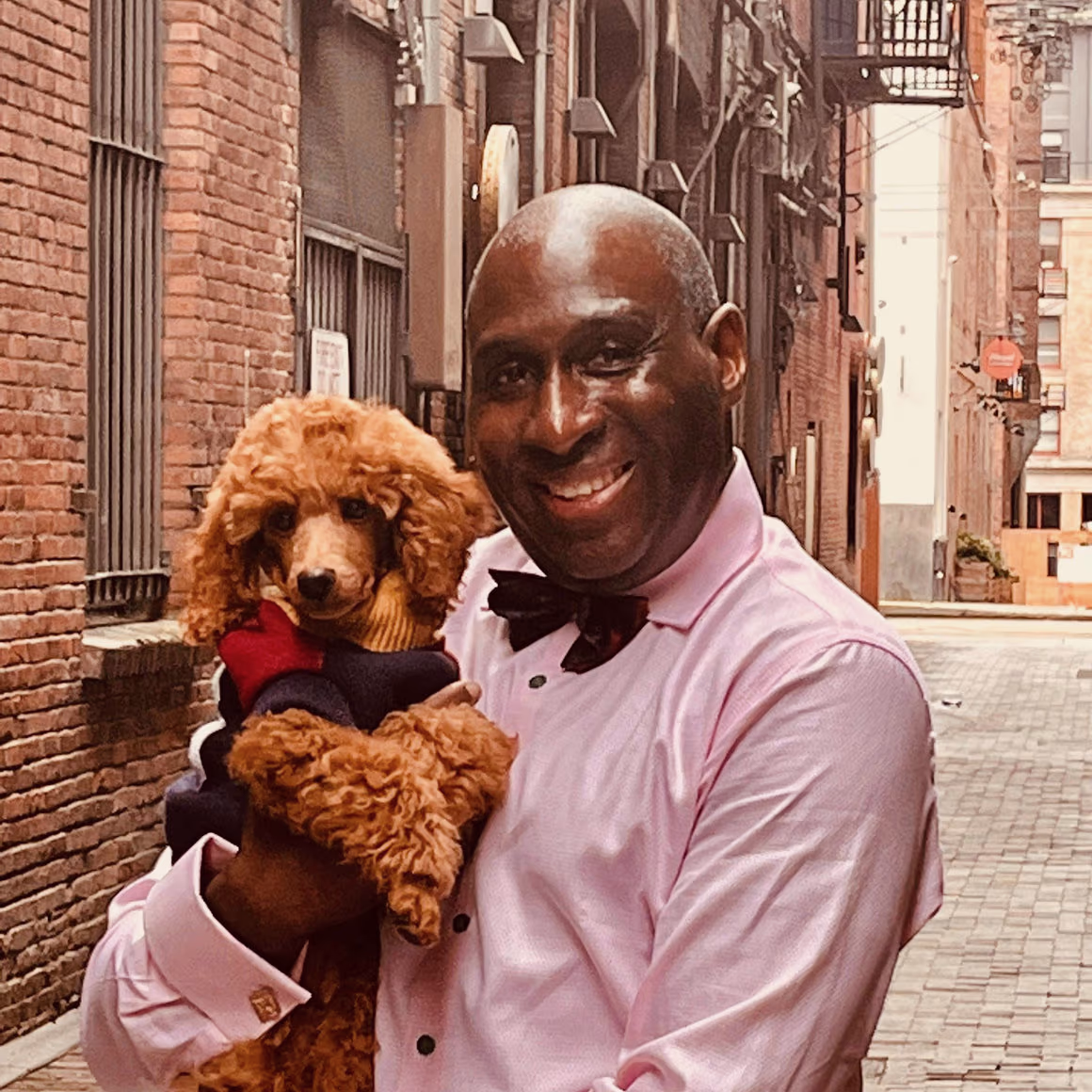 HRH Ritchard Wooley holding a poodle in an urban alleyway